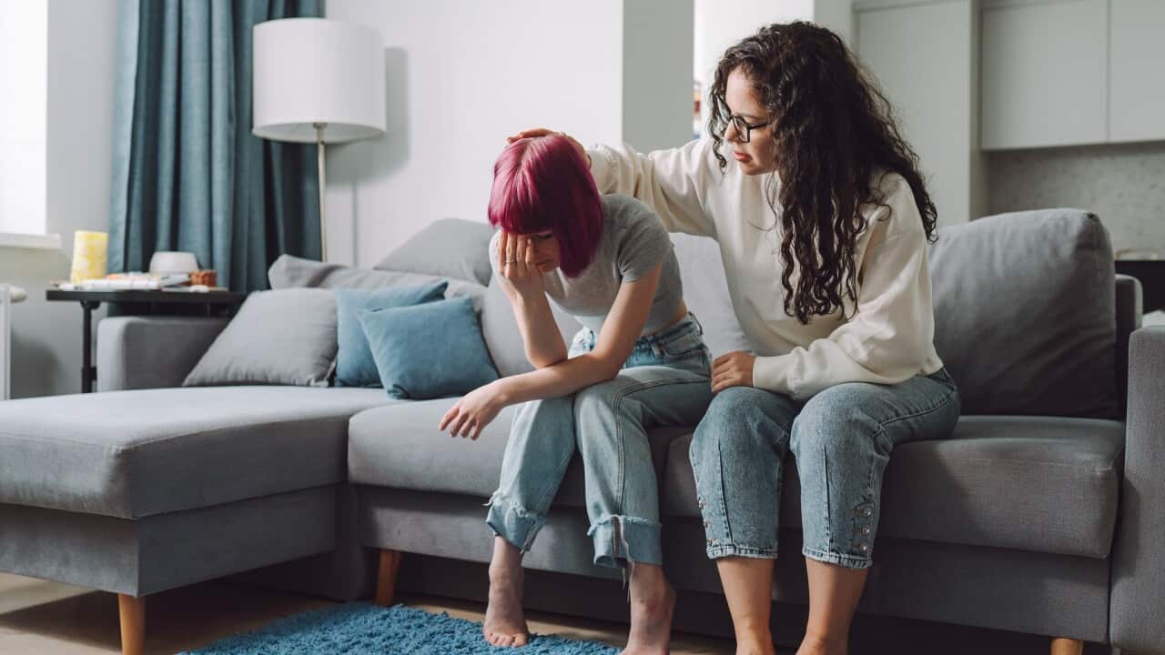 Feeling lonely and vulnerable. Teenage girl covering her face and crying on a couch, while her mother stroking her on a head