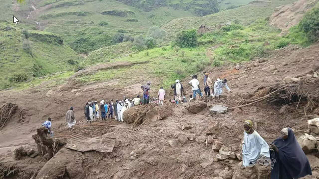 People walk past landslide damage atop a hill.