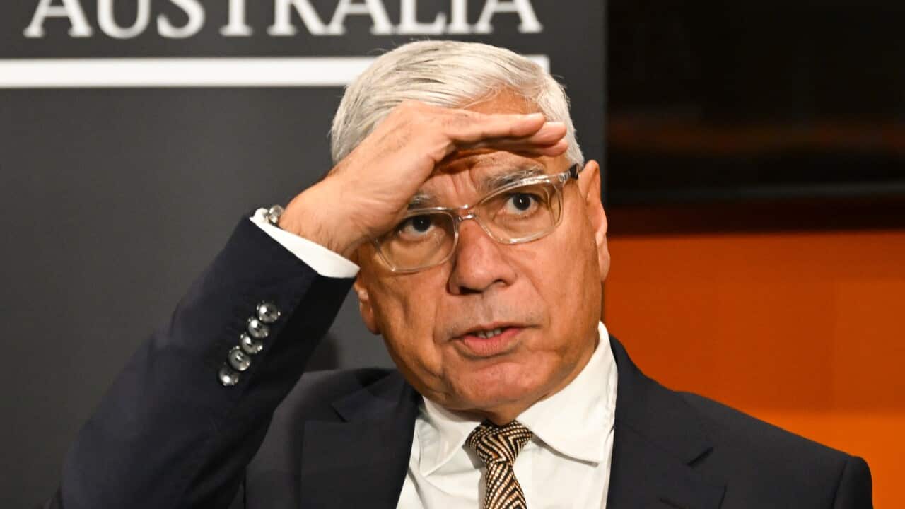 Warren Mundine wearing a suit and tie and holding his hand up on his forehead