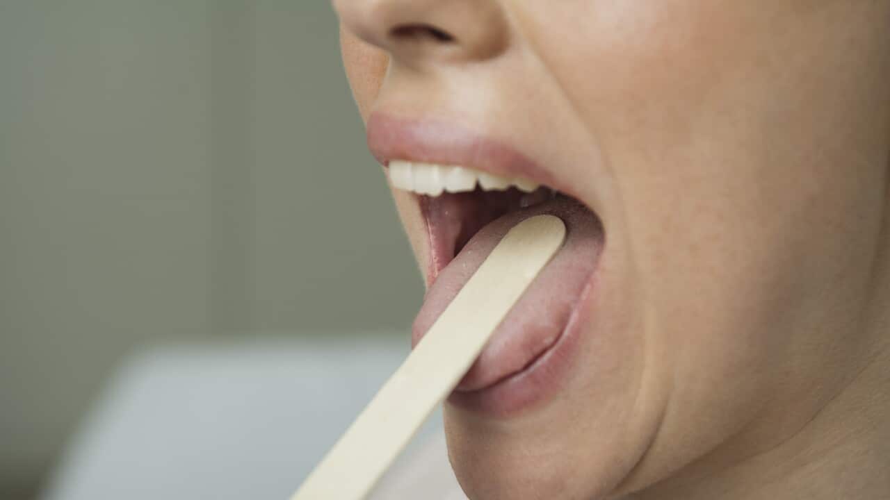 Woman having mouth examined with tongue depressor, cropped