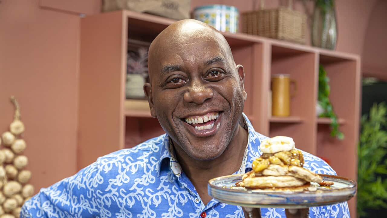 Man in vivid blue shirt covered in white squiggles smiles happily while holding a plate with a stack of pancakes.