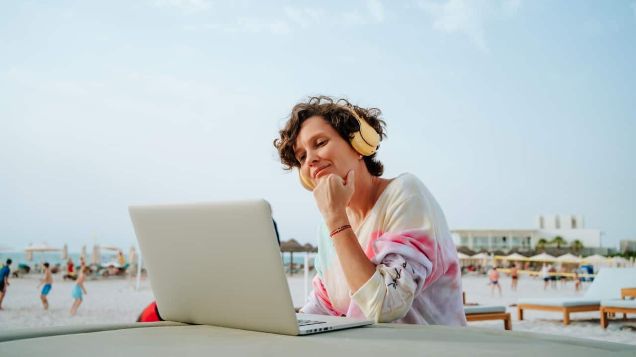 Coastal getaway with tech: smiling woman with wireless headphones enjoys the beach and video calls on the sunny beach