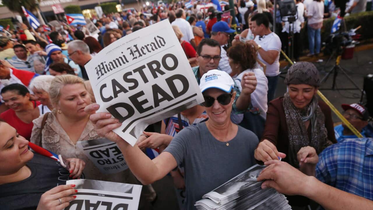 A woman hands out a special edition of the Miami Herald with the headline "Castro Dead," in front of the Versailles Restaurant in the Little Havana neighborhood