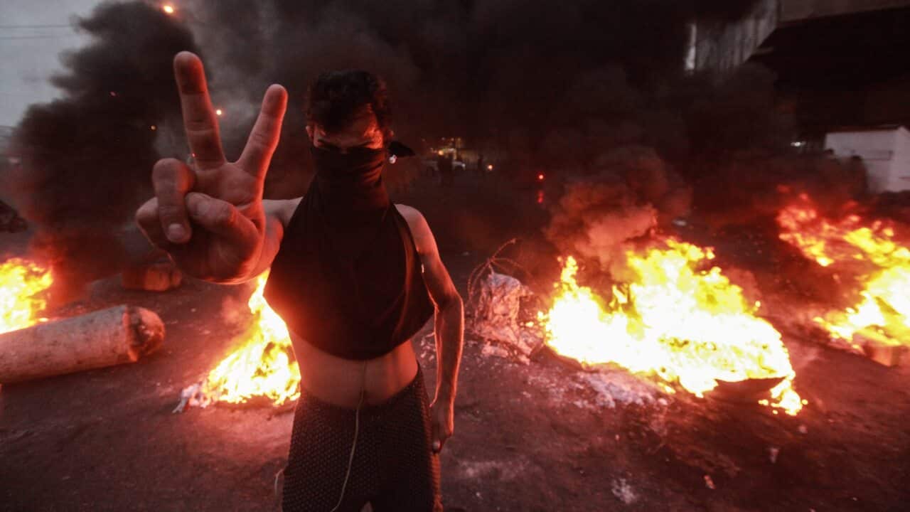 An Iraqi man gestures backdropped by a burning barricade during a violent anti-government protest.