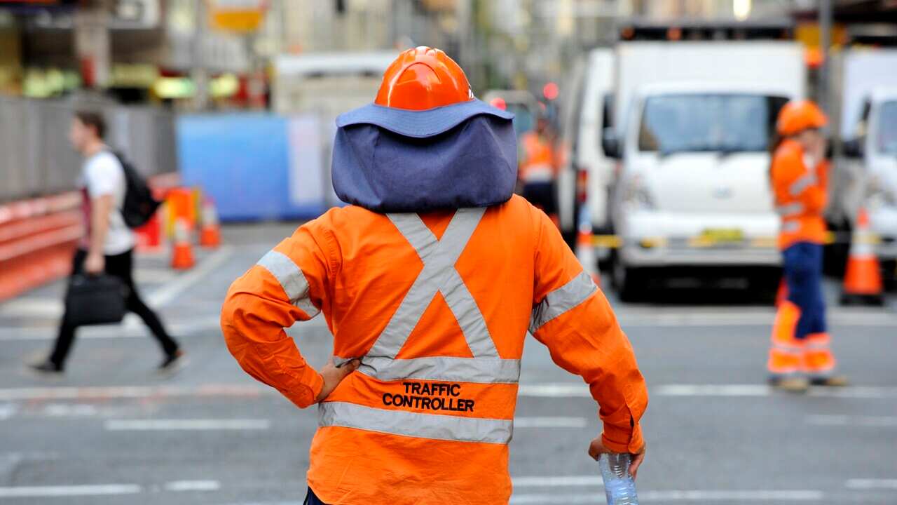 A traffic controller wearing bright orange looking away from camera