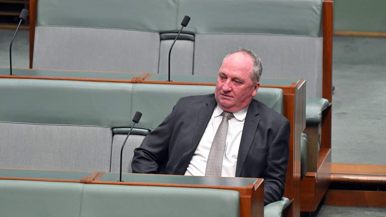 A man in a dark suit and tie sits looking downcast in a padded bench seat within Australia's House of Representatives.