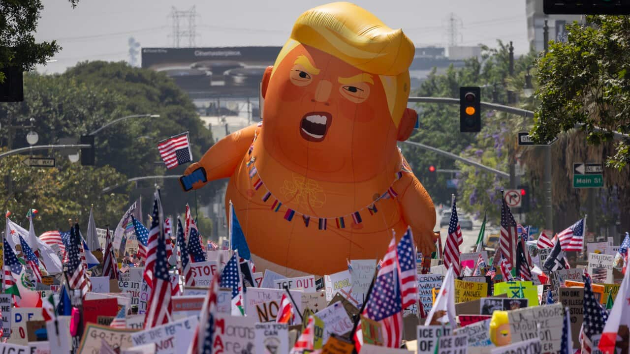 A huge inflatable balloon depicting Donald Trump as an angry baby floats above a dense crowd of protesters holding a multitude of American flags and signs.