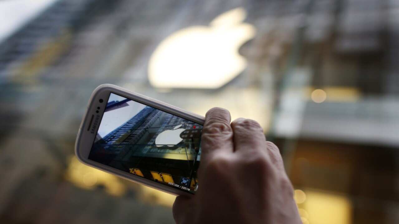 A passerby photographs an Apple store logo with his Samsung Galaxy phone on the morning iPhone 5 goes on sale to the public in central Sydney 