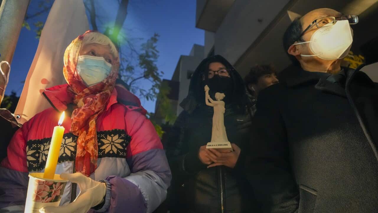 Three people hold candles and statues to commemorate the 1989 crackdown during a vigil outside the Chinese Consulate in Sydney.
