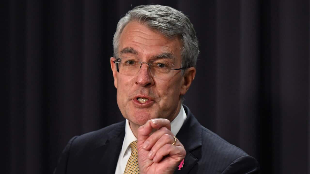 A man with grey hair, wearing glasses, a dark suit, which shirt, and yellow tie