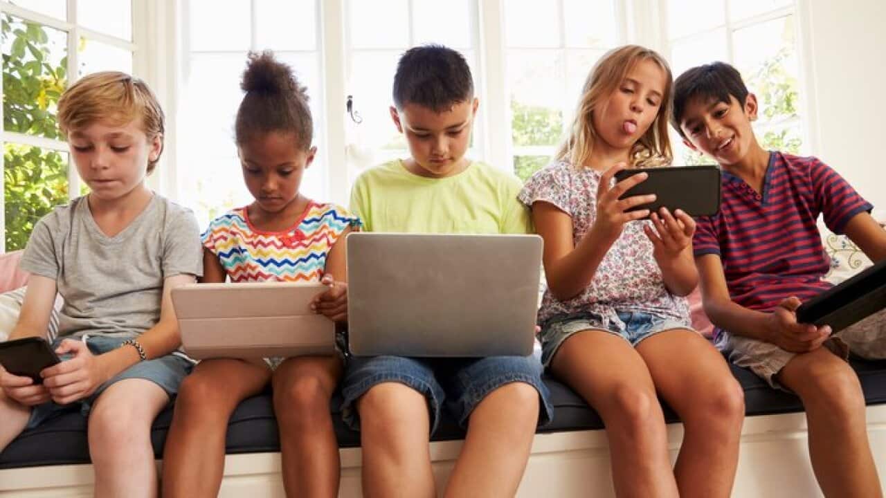 Group Of Children Sit On Window Seat And Use Technology