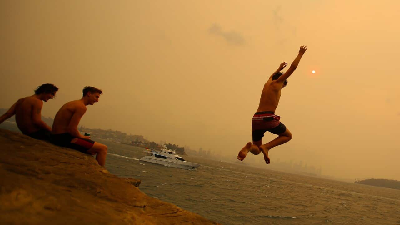 Smoke haze from bushfires blankets the Sydney CBD as beachgoers Jump from a cliff in Nielsen Park during hot weather in Sydney, Saturday, December 21, 2019. (AAP Image/Steven Saphore) NO ARCHIVING