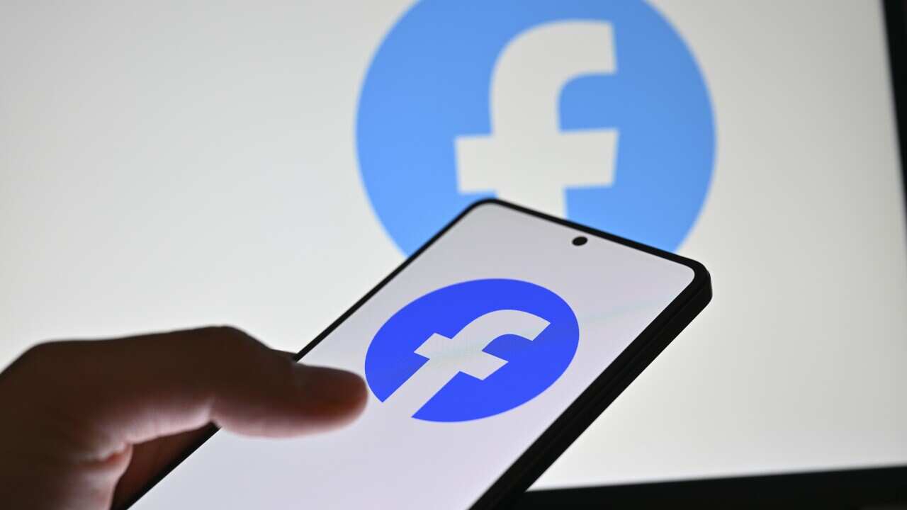 A person using a smartphone. On the screen of the device is the Facebook logo.