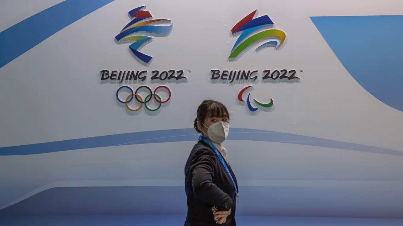 A woman wearing a protective face mask walks past the logos of the Beijing 2022 Olympic and Paralympic Winter Games.