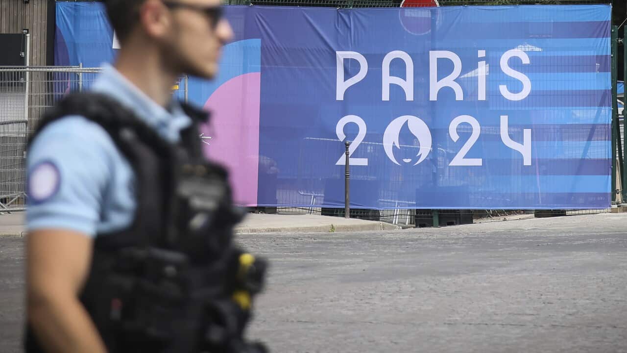 A policeman next to a poster that reads "Paris 2024".