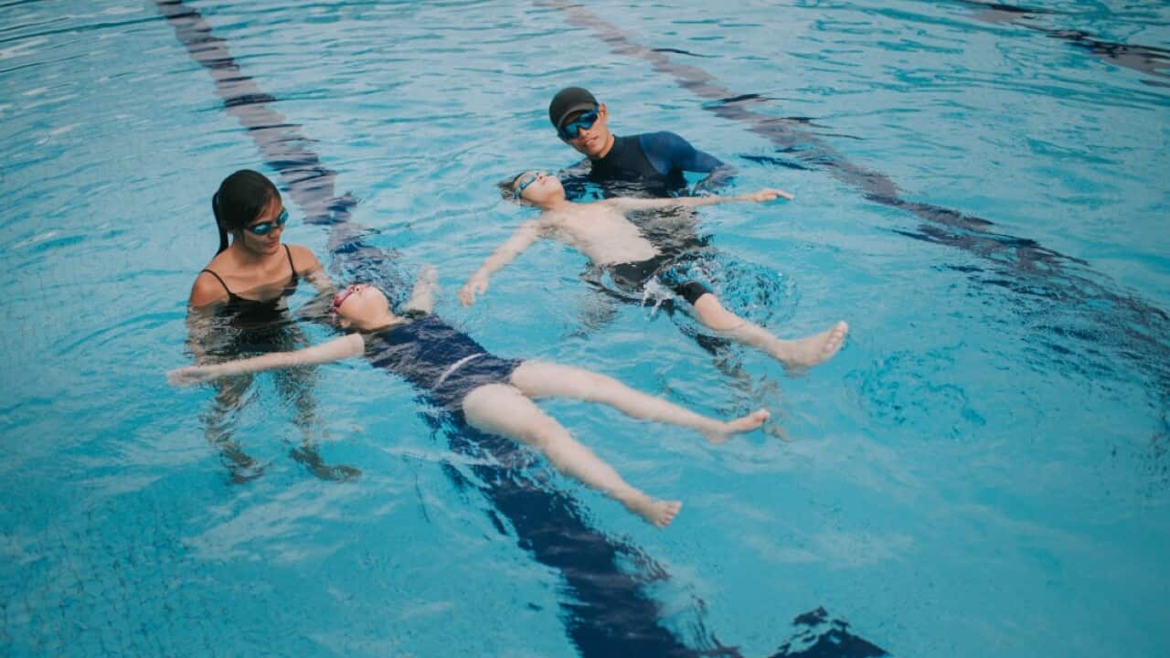 2 asian chinese coaches instructors teaching their young student floating on water in swimming pool