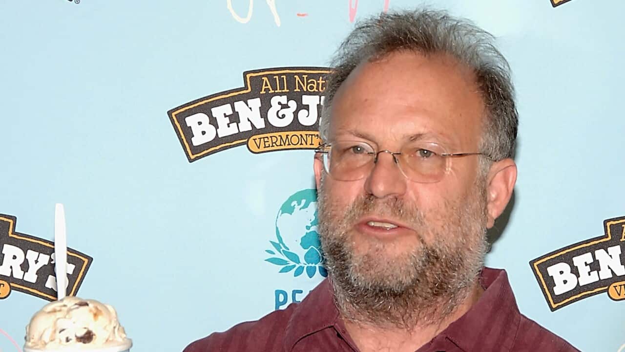 A man holding a cup of ice cream, in front of a mural with the Ben and Jerry's logo.