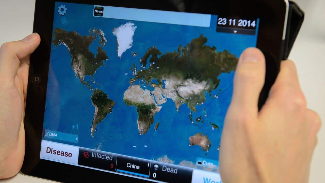 A man holds a tablet device showing a screen from the video game "Plague Inc"