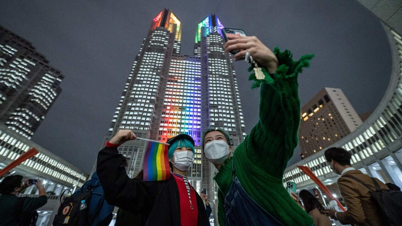 Two Japanese women in front of a Tokyo building with rainbow lights.