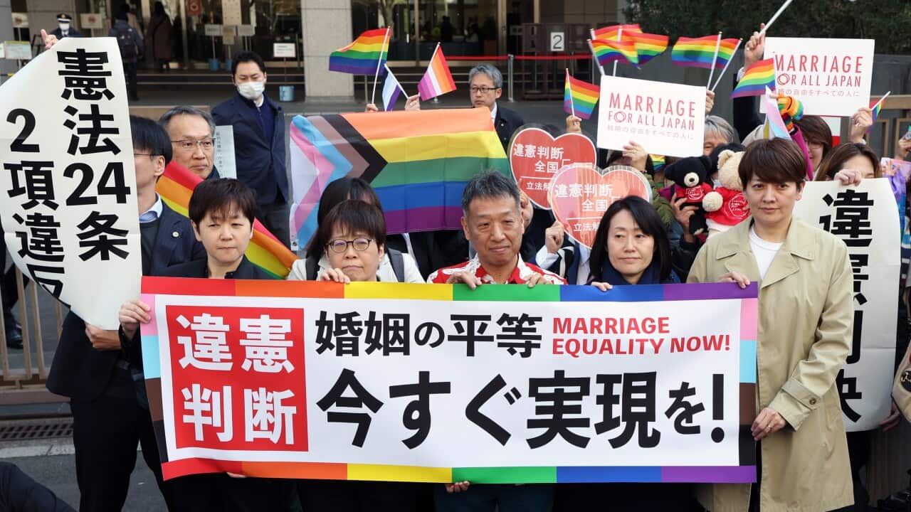 A group of people stand outside a courthouse holding banners
