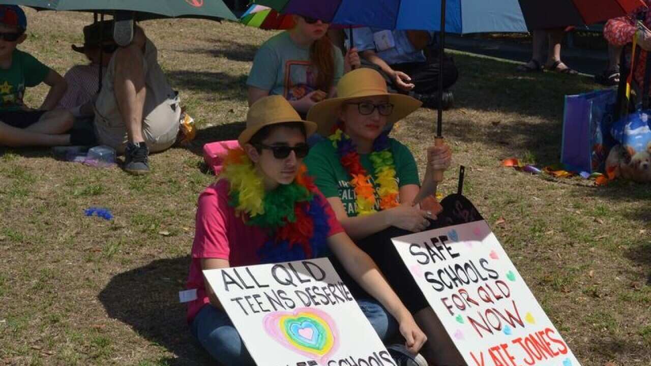 Members of the public hold signs supporting the Safe Schools program.