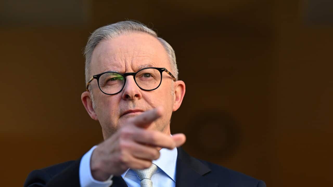 A man wearing a suit and tie points his index finger at a press conference