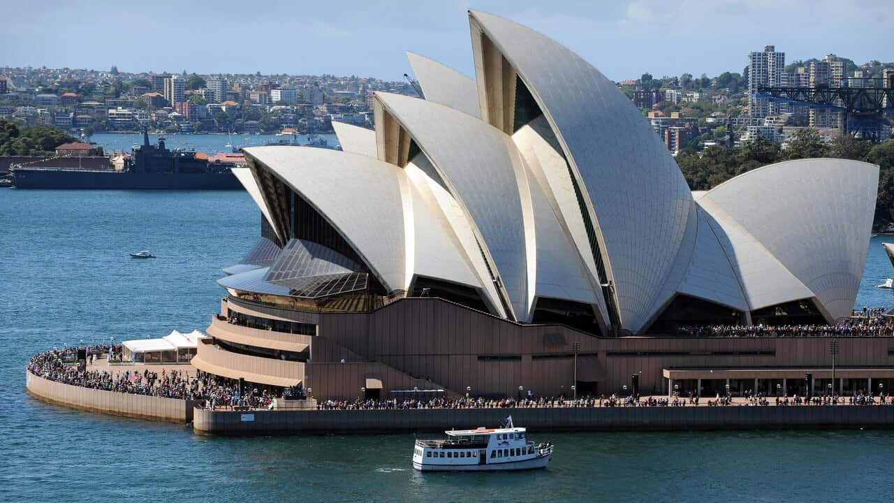 Crowds line the forecourt of the Sydney Opera House as warships sail into Sydney Harbour.