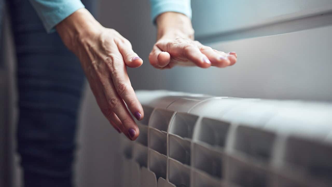 A woman heating her hands on a radiator.