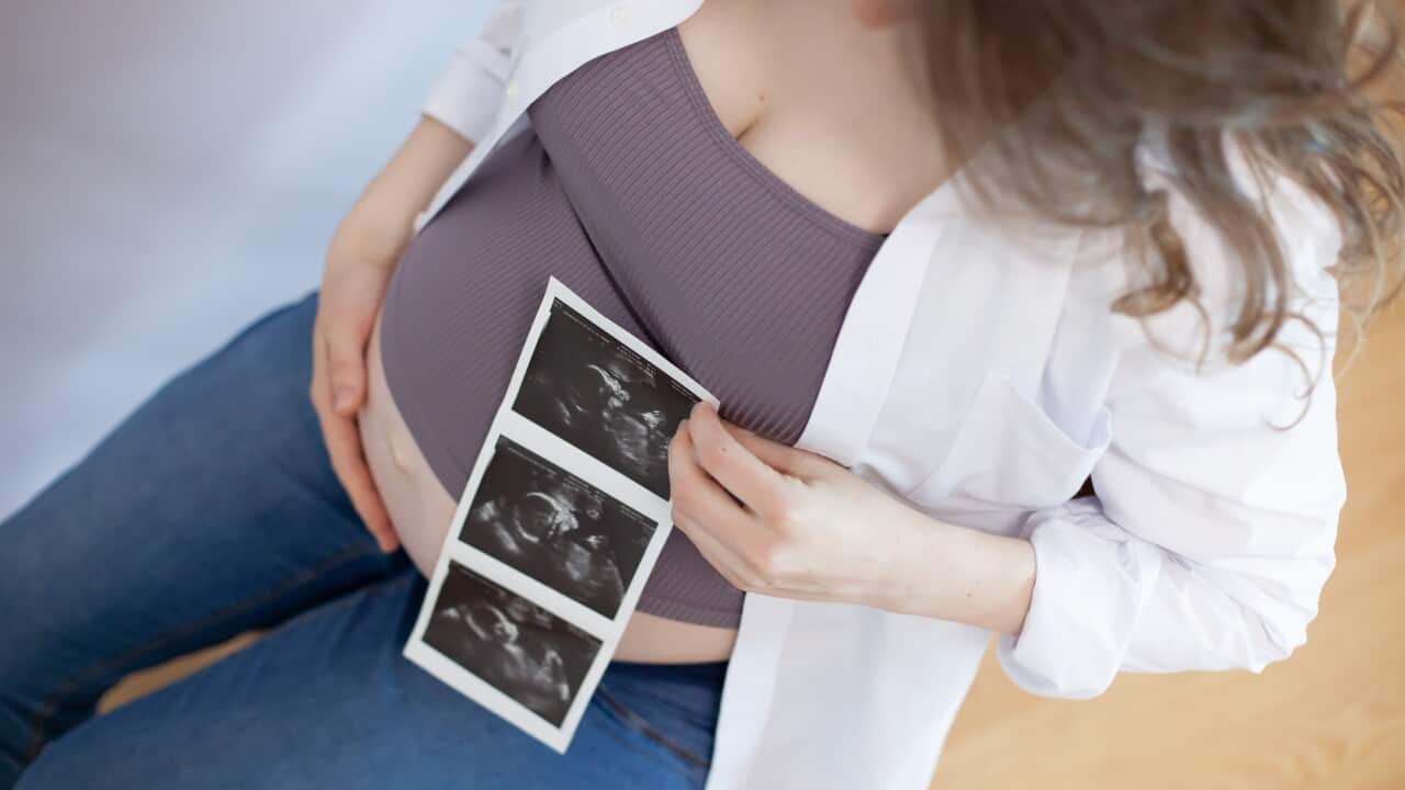 A pregnant woman is shown holding an ultrasound picture showing the baby in her hand.