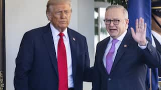 Donald Trump standing next to Anthony Albanese, who is waving a hand. They are in front of a white wall.