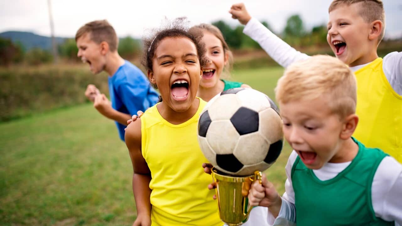 A group of children with cup prize standing outdoors on football pitch.