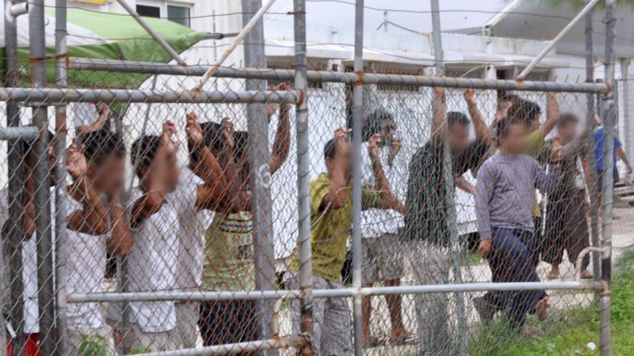 Asylum seekers stand behind a fence at Manus Island