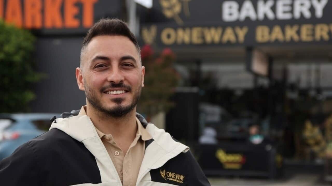 Man standing with his arms on his hips outside a bakery.
