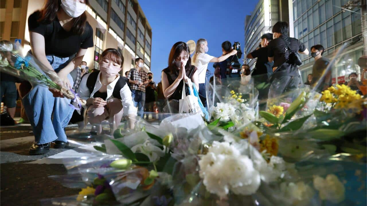 People praying behind flowers laid on the ground.