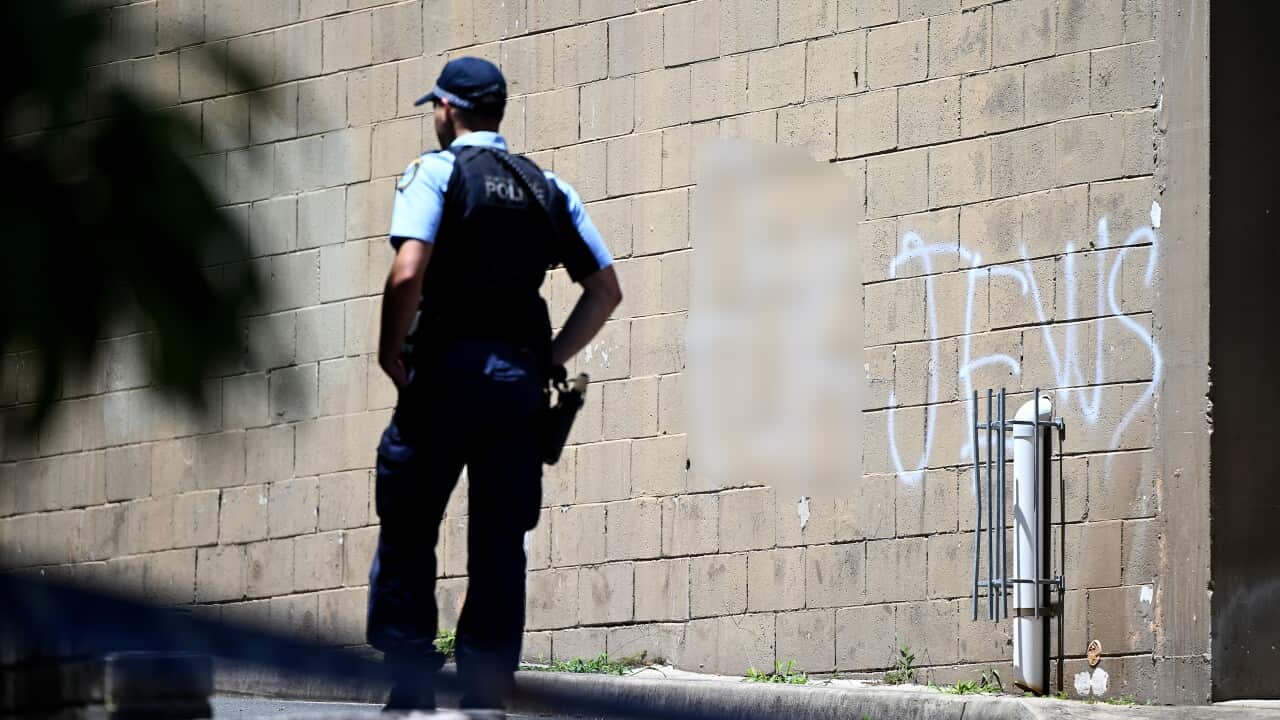 A policeman standing in front of a vandalised wall.