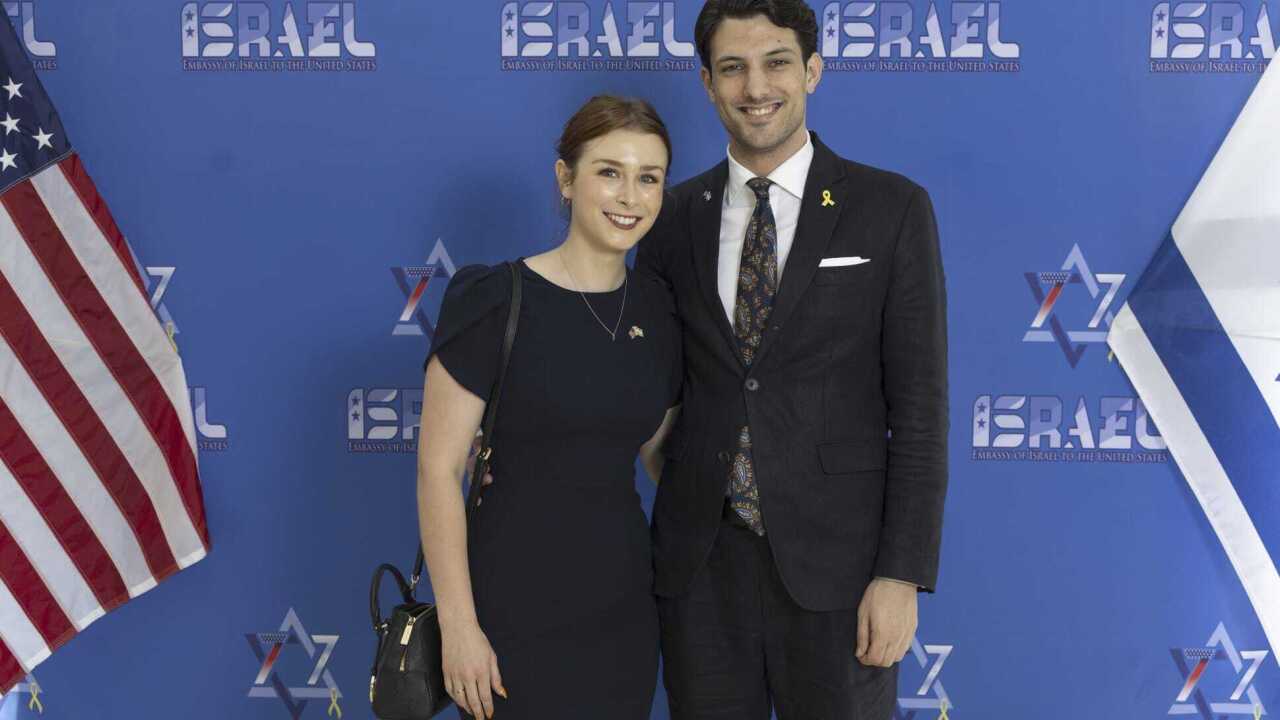A woman and man in black formal outfits standing in front of a blue background