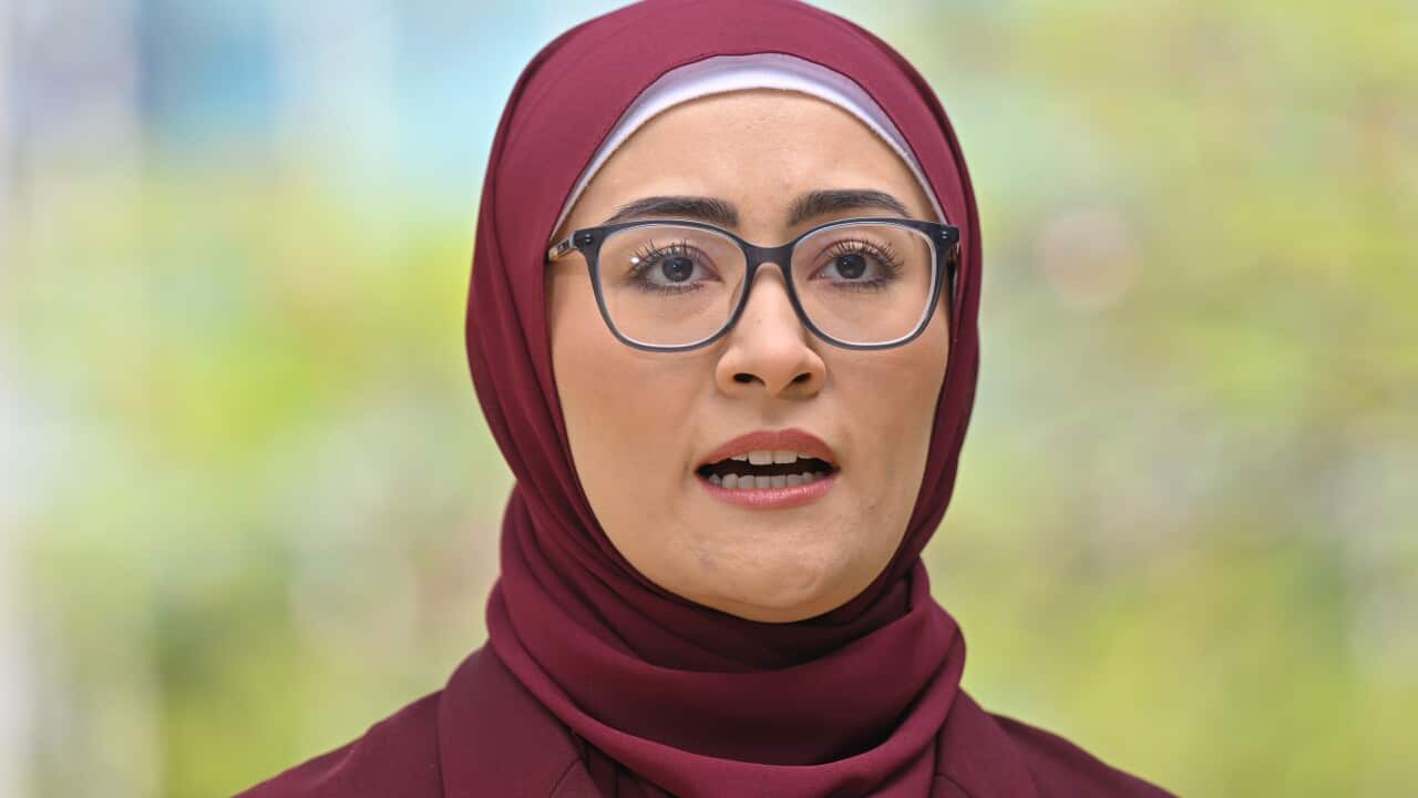A woman wearing glasses speaking while standing outside.