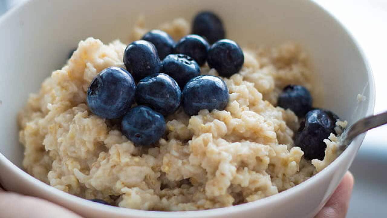 Person holding bowl of oats with blue berries