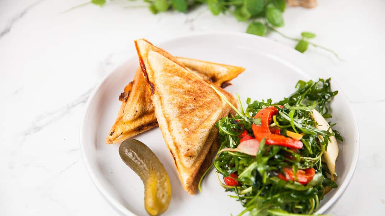 Two golden jaffle triangles sit on a white plate with a small pile of saad and a pickle alongside