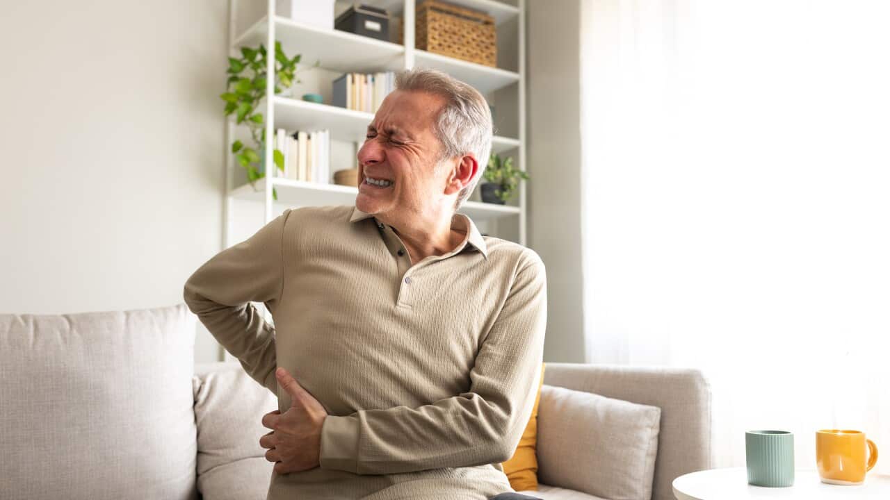 Senior man suffering from back pain while sitting on sofa at home