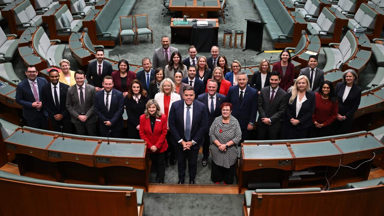 Men and women standing in the house of representatives, with their hands in front of them.