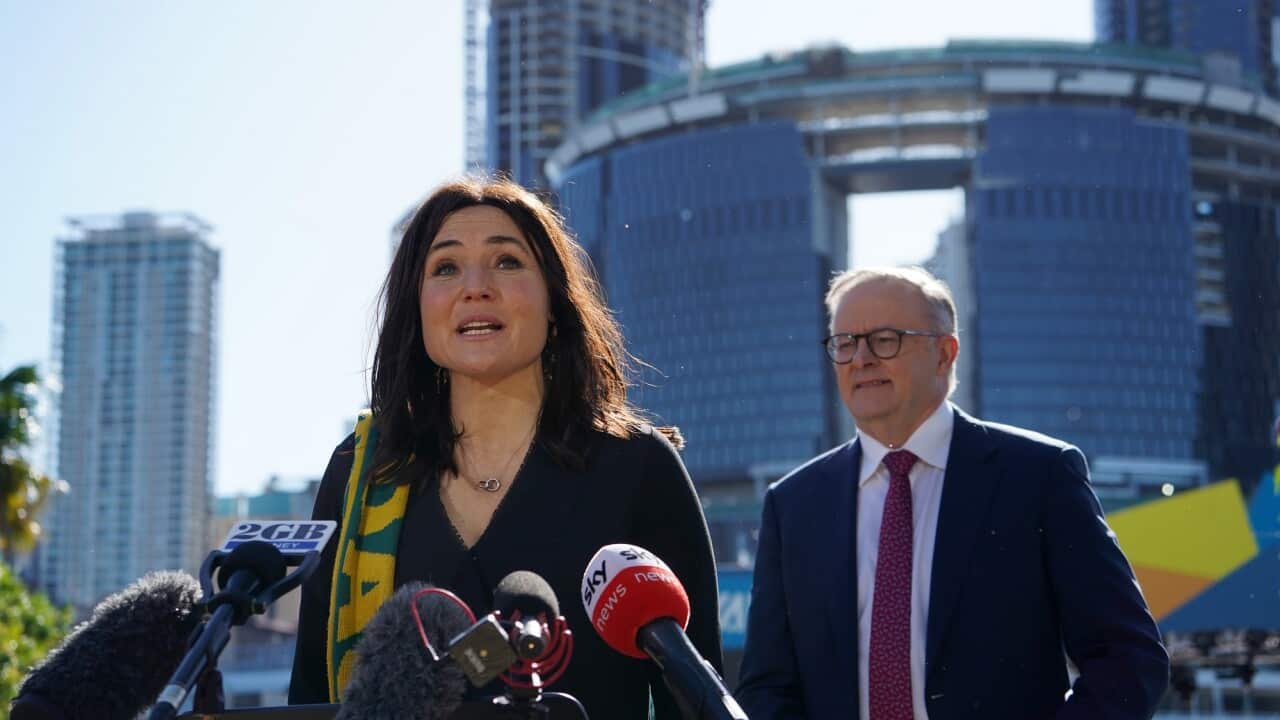 Tal Karp stands in front of microphones. Anthony Albanese can be seen behind her on the right.