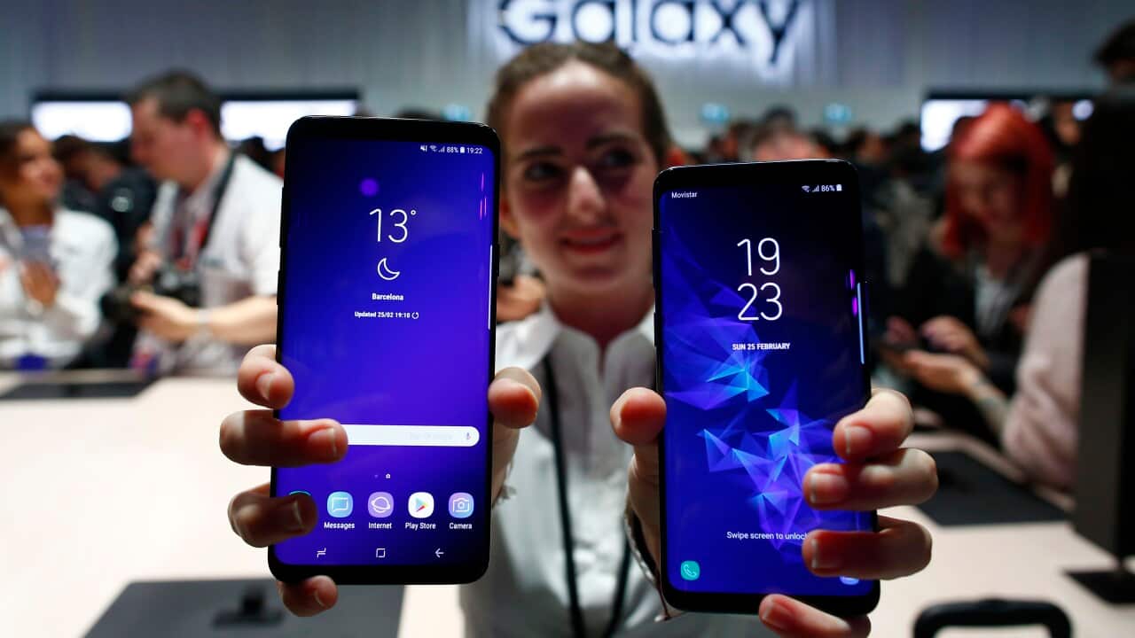 A woman at a Samsung Galaxy store carrying two S9 models facing outwards