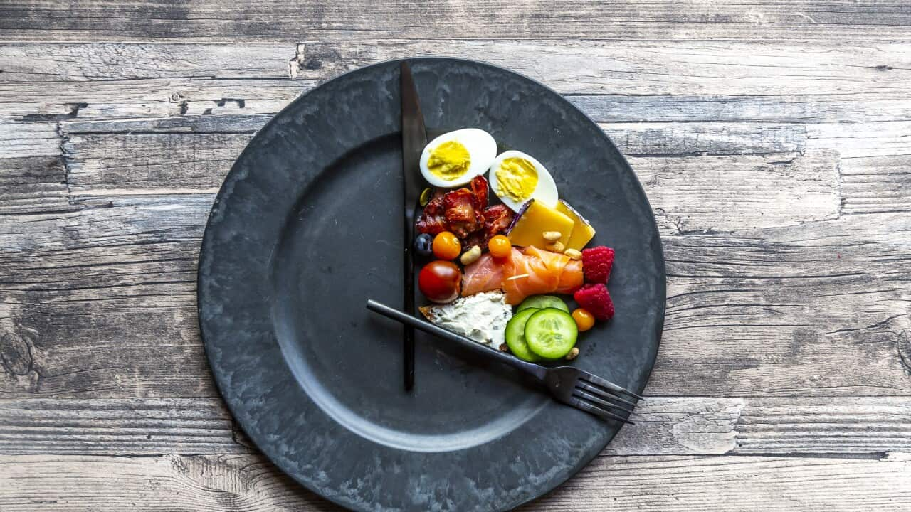 A selection of food on a plate, with a knife and fork positioned to resemble a clock