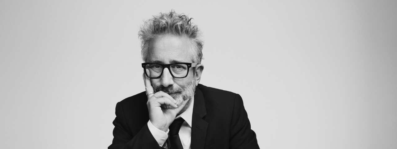 David Baddiel sits at a table wearing a suit