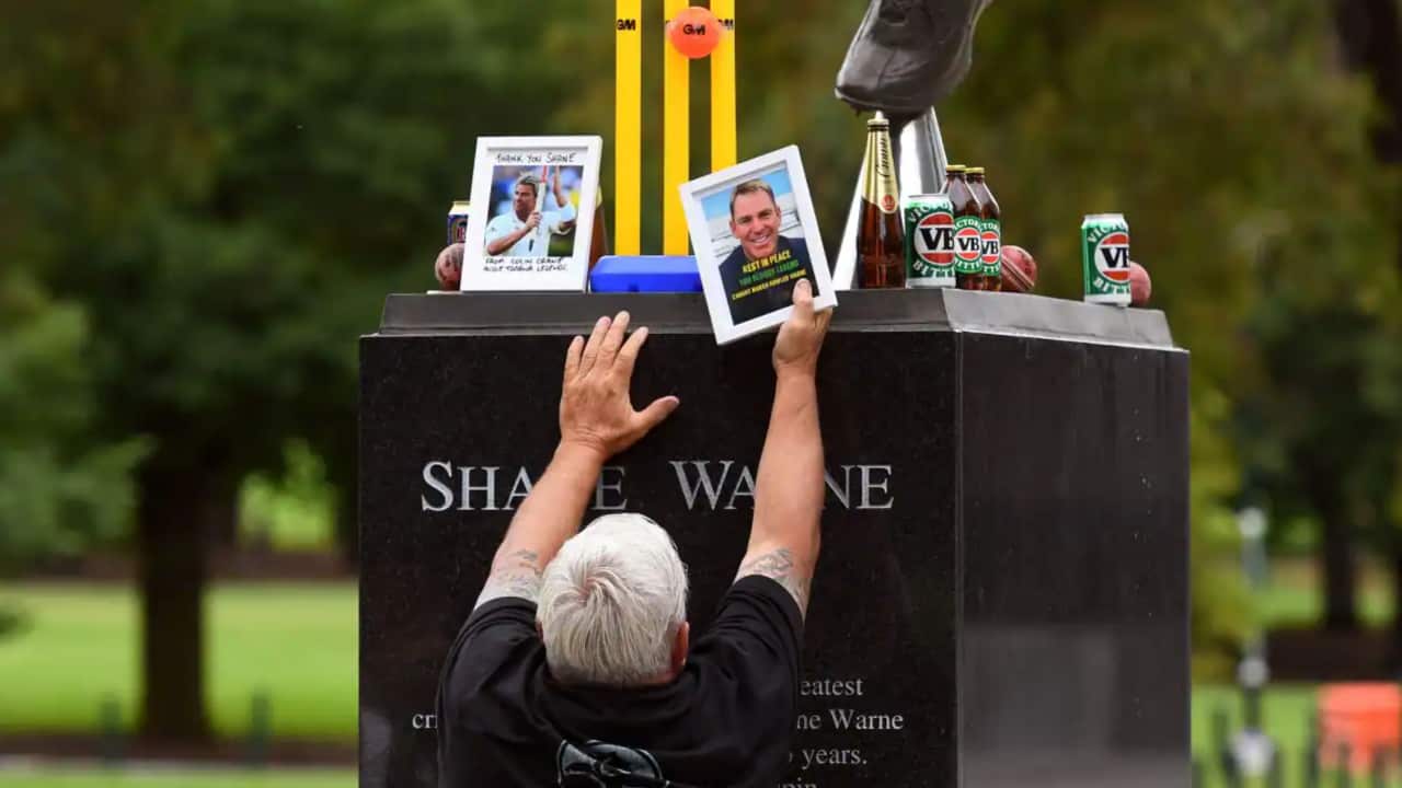 A man places photos at the base of a statue of former Australian cricket great Shane Warne at the Melbourne Cricket Ground in Melbourne.