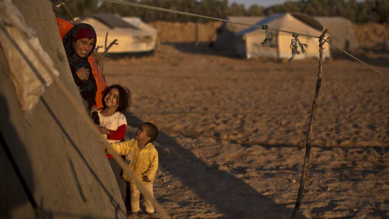 A Syrian refugee woman and her children stand at the doorway of their tent