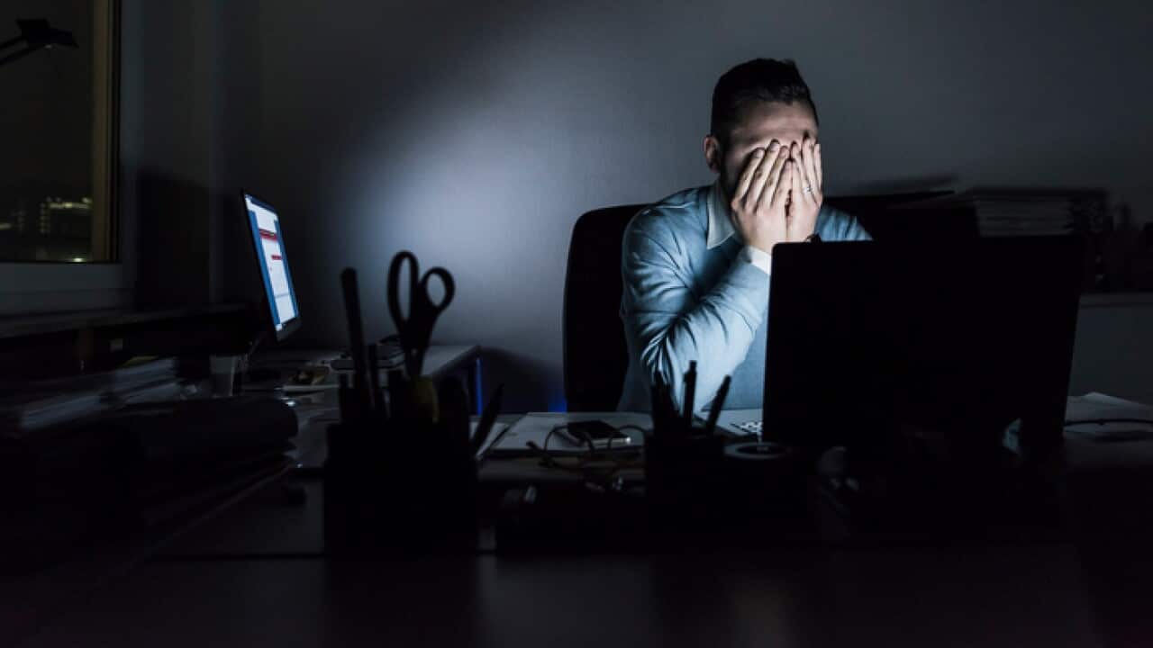 A stressed, exhausted businessman sitting at his desk in an office at night