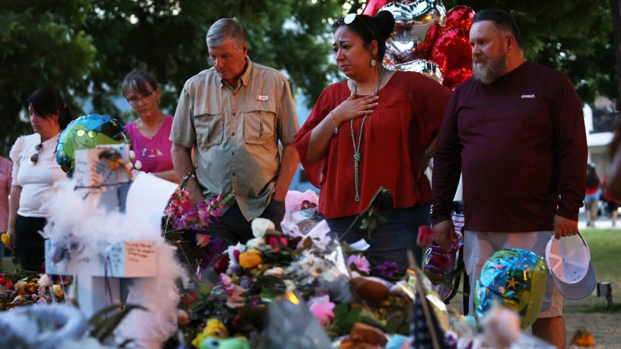 Two men and a woman grieve as they look at photos and flowers of victims killed in a school shooting.
