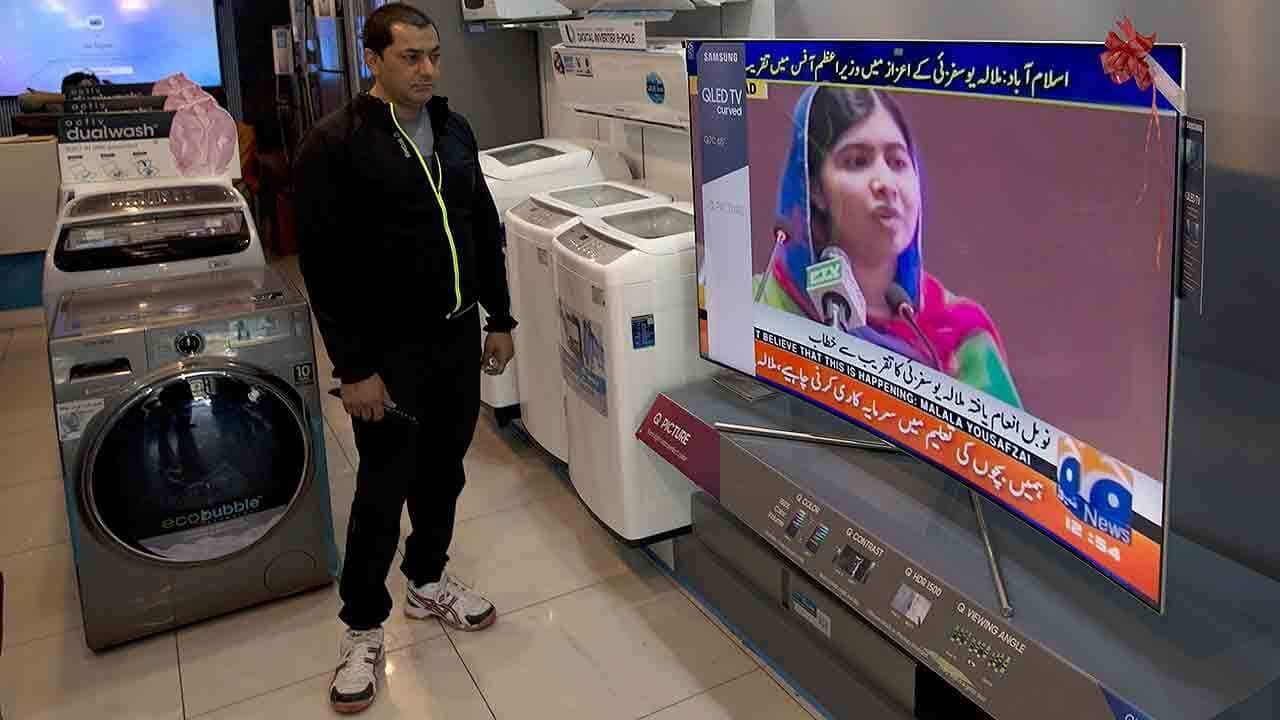 A Pakistani shopkeeper listens to Malala Yousafzai addressing a reception at prime minister house in Islamabad.